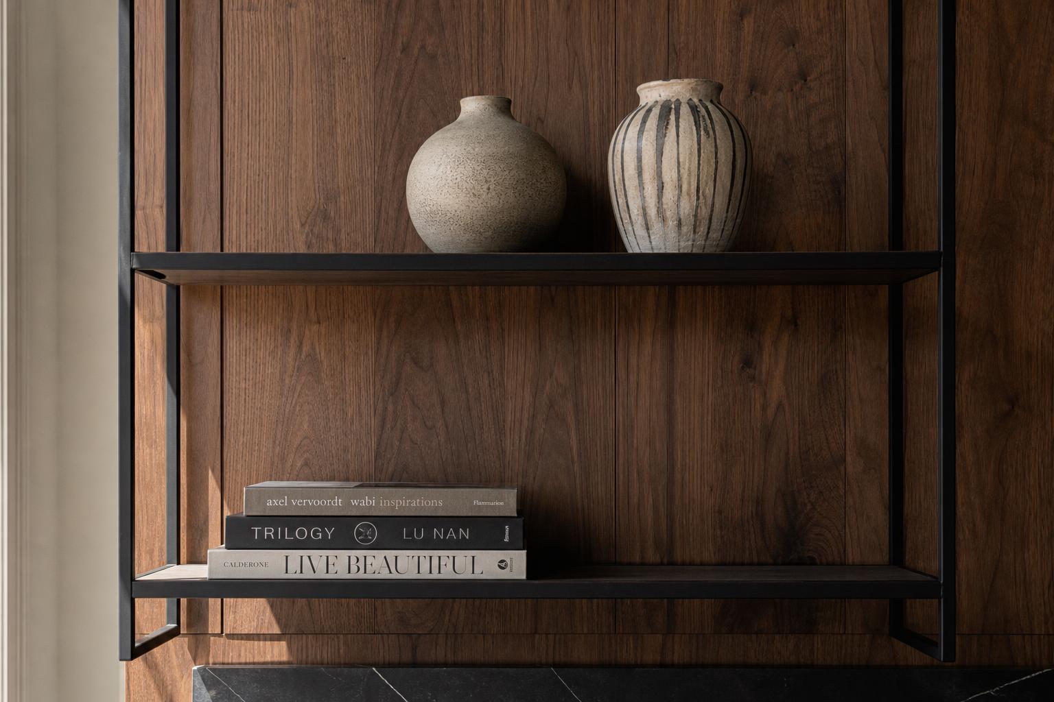 Blackened steel shelving against warm walnut paneling styled with ceramics